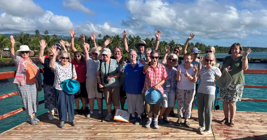 Smiling tour group waving on tropical wooden jetty
