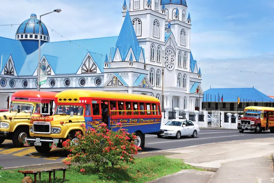 Colourful buses pass a blue-roofed church