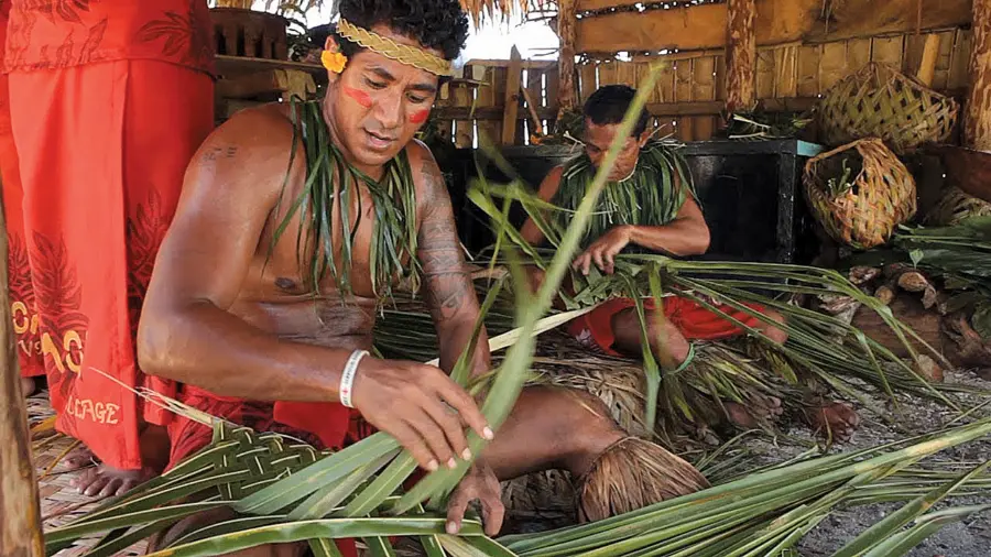 Indigenous men weaving palm leaves inside a thatched hut