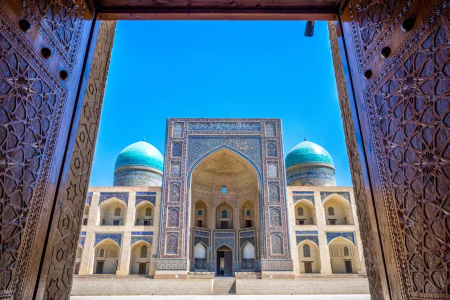Ornate gateway framing tiled mosque with turquoise domes