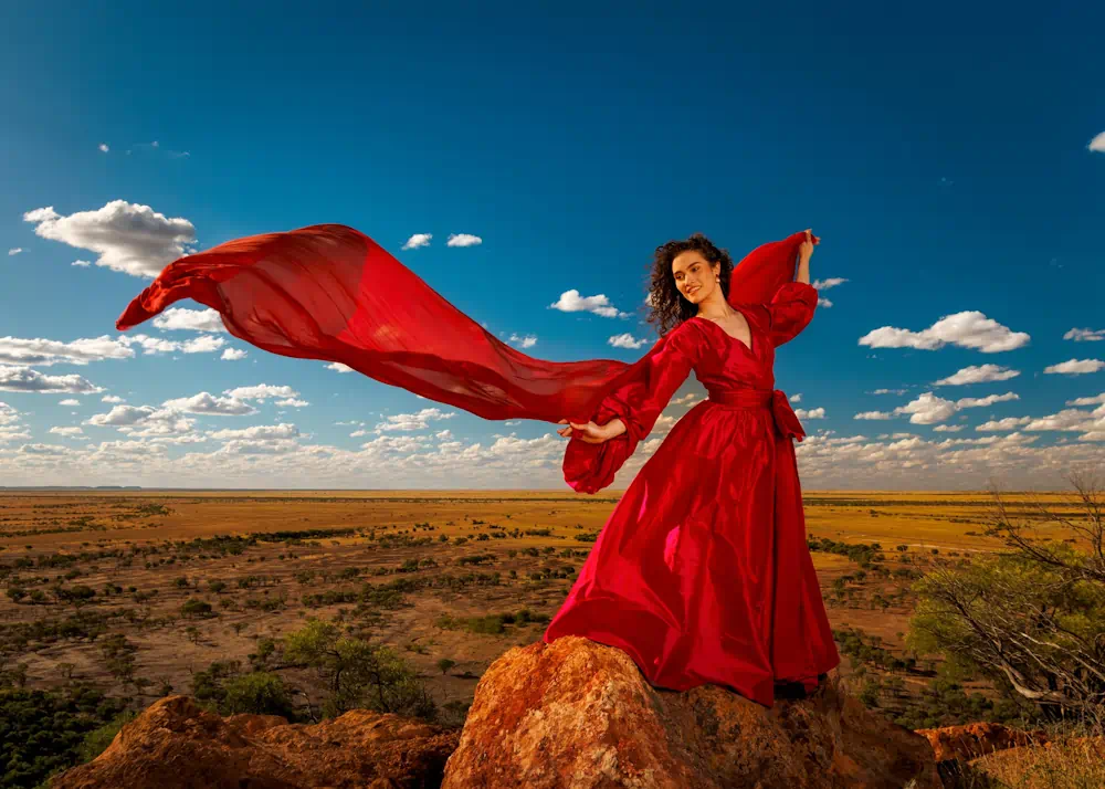 Woman in flowing red dress atop outback rock